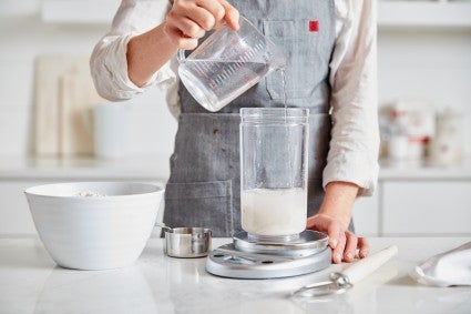 Sourdough starter in a glass jar on a scale being fed with water.